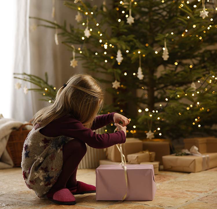 Een klein meisje zit voor de kerstboom en pakt een cadeautje uit.