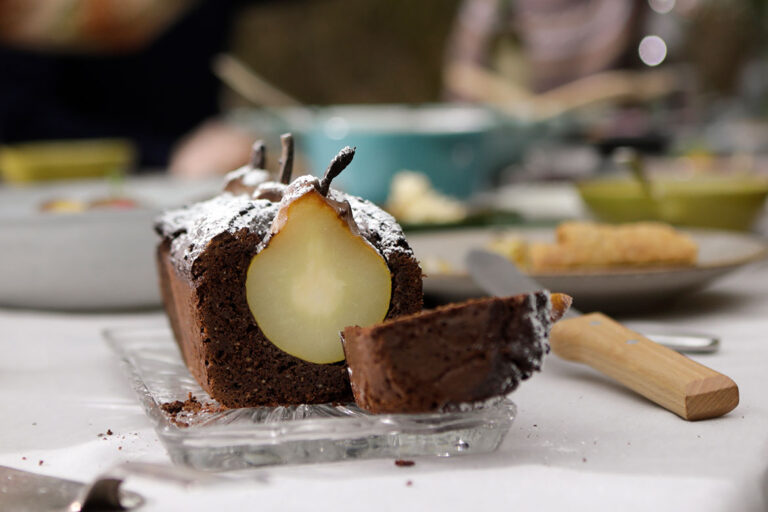 Een rode wijncake met verzonken peren staat aangesneden op een gedekte tafel.