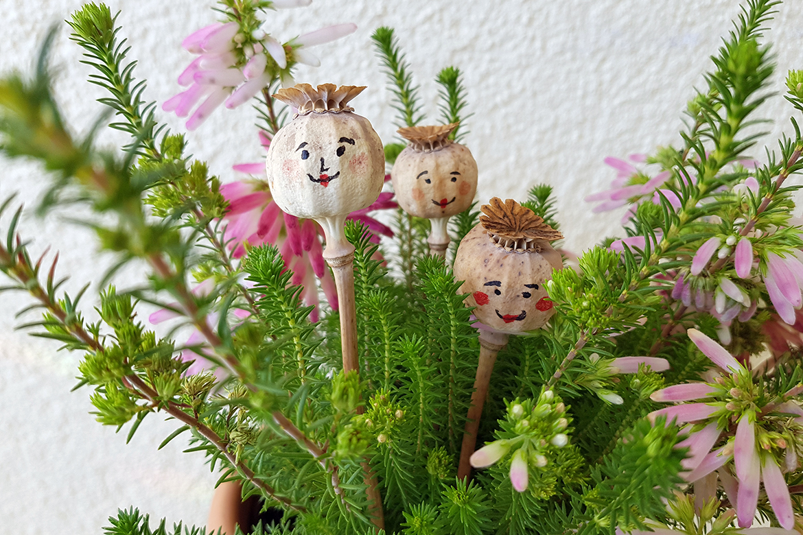 Drie zelfgemaakte bloemenmeisjes van papaverbollen sieren een bloempot.
