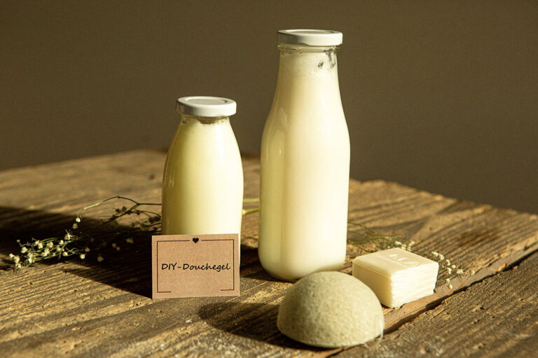 Twee flessen zelfgemaakte douchegel staan op een houten tafel, een beschreven etiket leunt tegen de kleine fles.