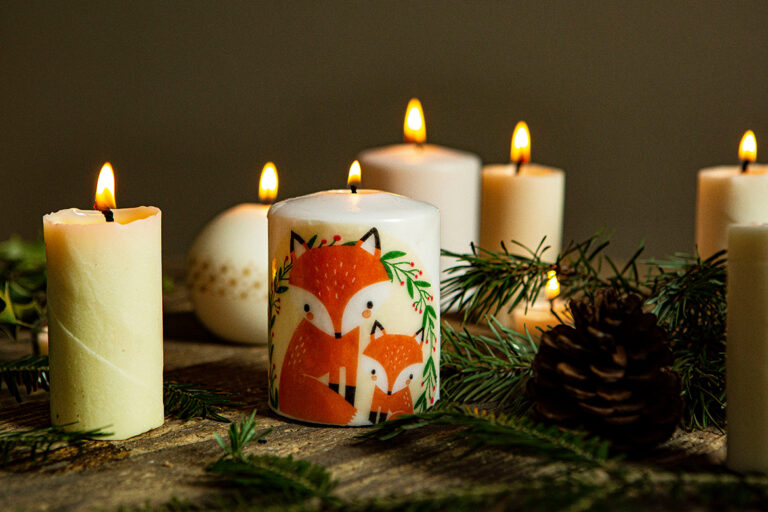 Vele brandende kaarsen staan op een tafel, de voorste kaars is versierd met een vossenmotief.