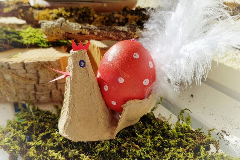 De haan zit op mos en draagt een rood ei met witte stippen.