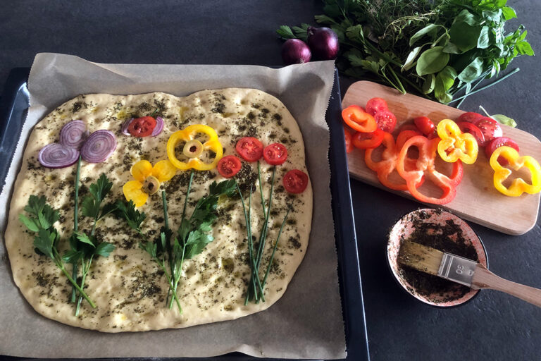 Een zelfgemaakte focaccia is belegd met groente in de vorm van bloemen.