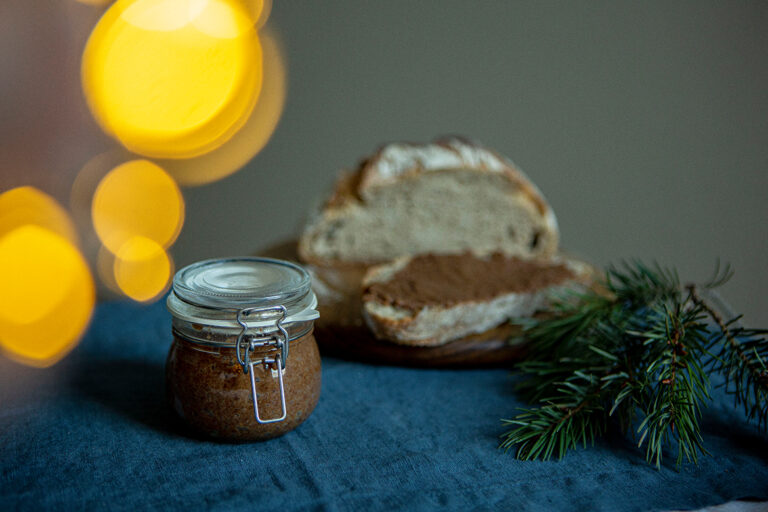 De geroosterde amandelspread zit in een klein potje voor een plank met daarop besmeerd brood.