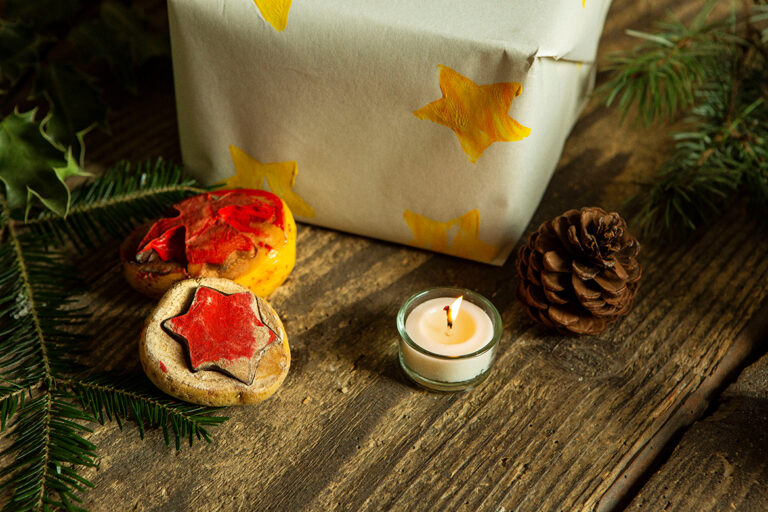 Zwei Kartoffelstempel liegen vor einem eingepackten Geschenk, bei dem das Papier mit Kartoffeldruck verziert wurde.