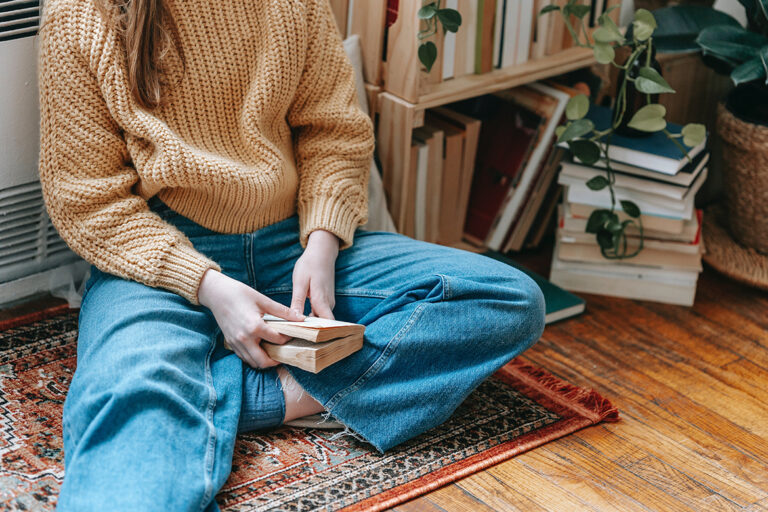 Een meisje zit met haar benen gekruist op een tapijt met een boek in haar hand en draagt een eco jeans.
