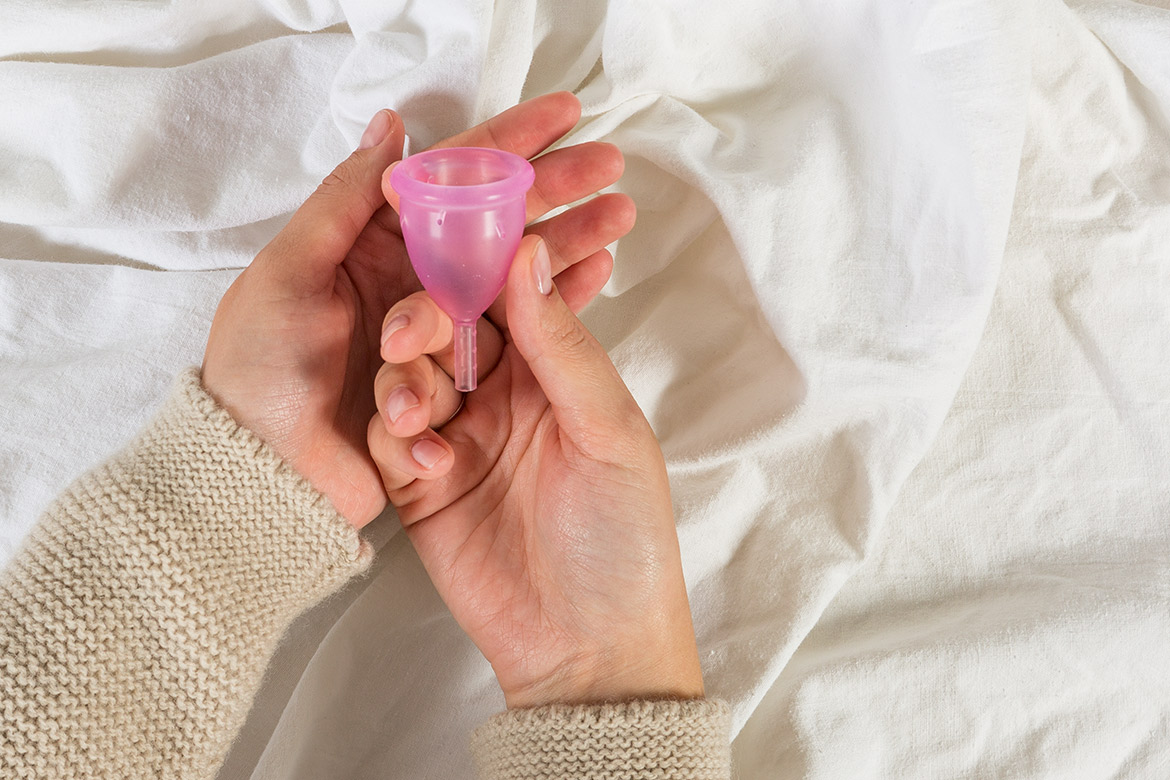 Twee handen houden een roze menstruatiecup vast