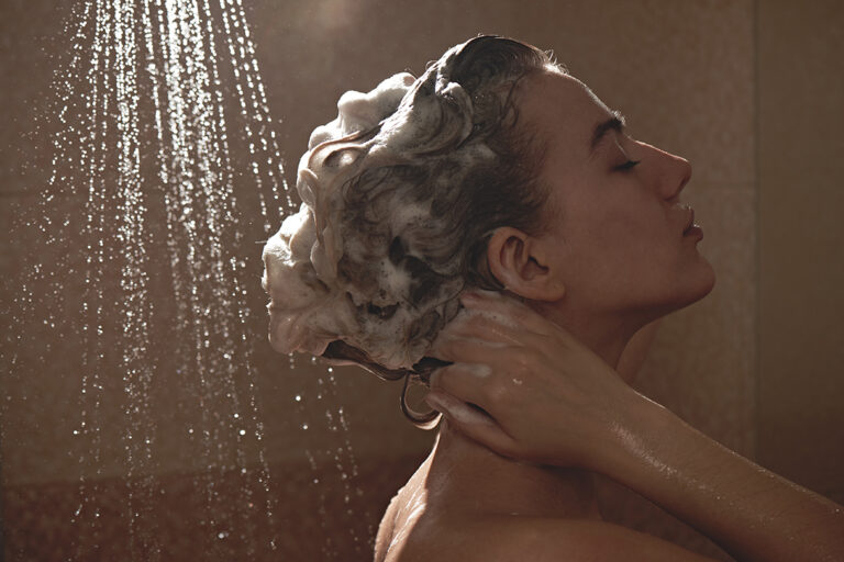 Een vrouw staat met ingeschuimde haren onder de douche.