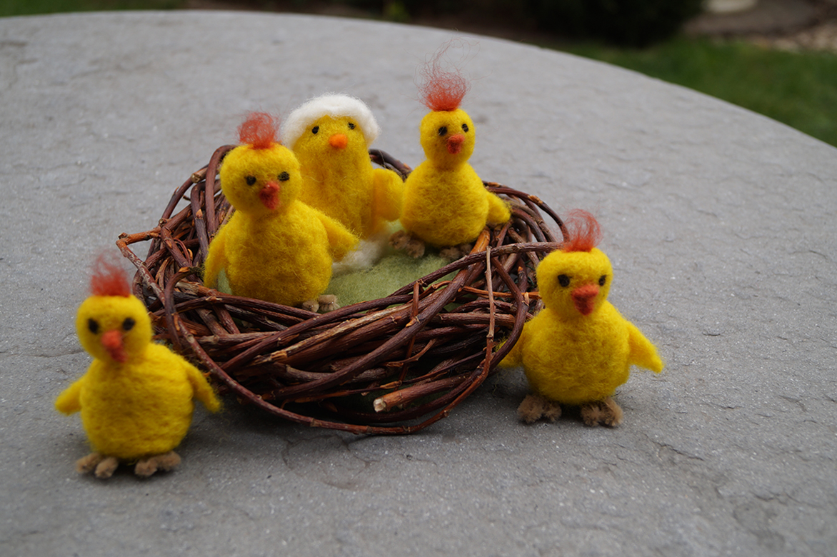 In en rond het vogelnestje zitten verschillende gele kuikens van vilt.