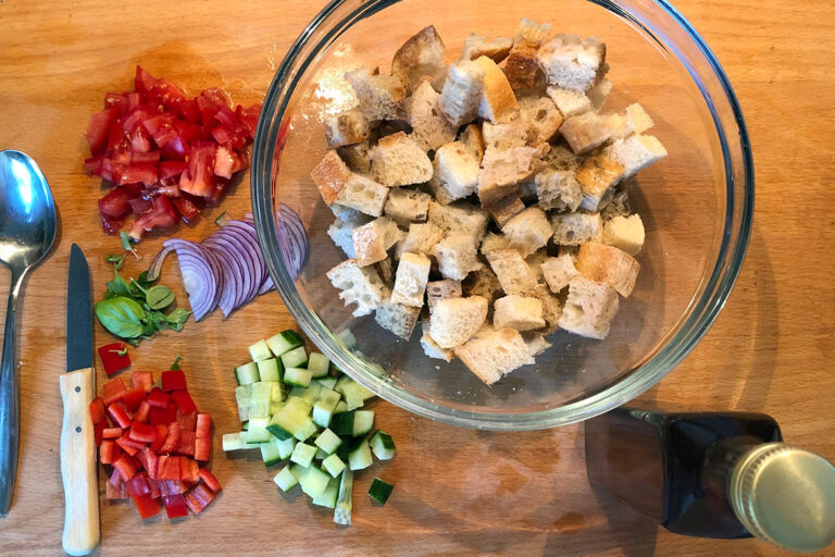 De ingrediënten voor de panzanella liggen klaar op het houten aanrecht, het brood ligt al in een kom.