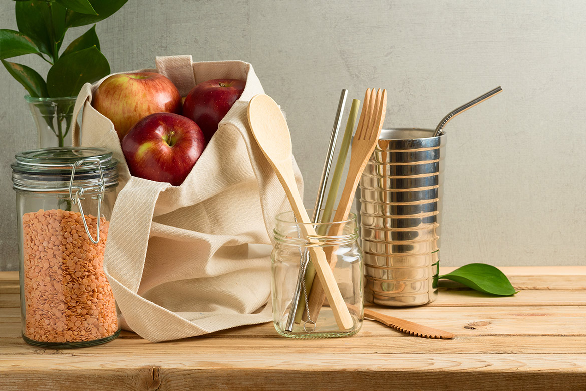 Rode linzen in een glas, rode appels in een katoenen zak, houten bestek en roestvrijstalen beker met roestvrijstalen rietje op een houten tafel.