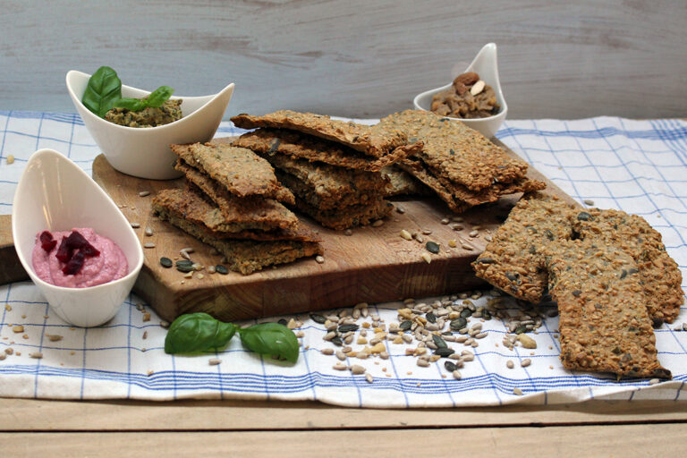 Zelfgemaakt knäckebröd ligt op een houten plank, met daarnaast dips in kleine schaaltjes.