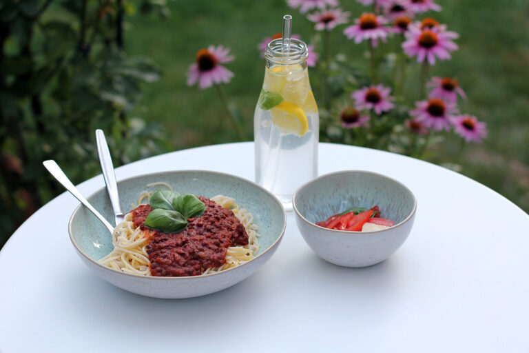 Een bord spaghetti met veganistische linzenbolognese samen met een verfrissend drankje en salade.