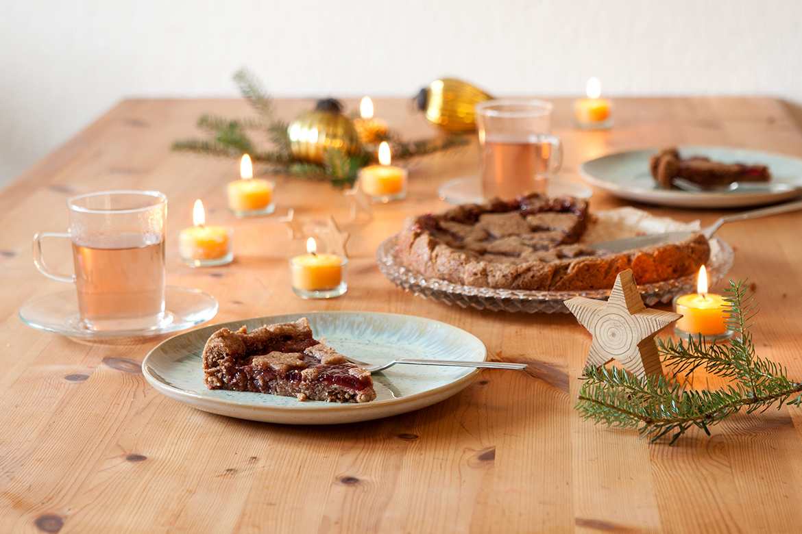 De veganistische Linzertaart staat aangesneden op een feestelijk gedekte tafel.