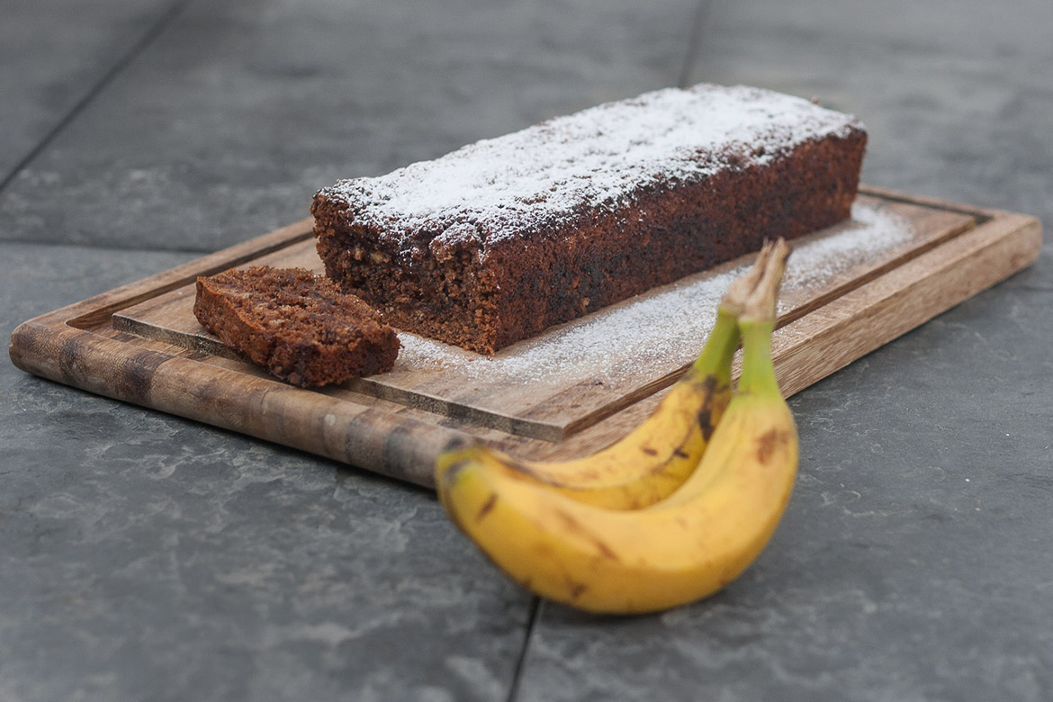 Bananenbrood ligt op een snijplank met 2 bananen ernaast