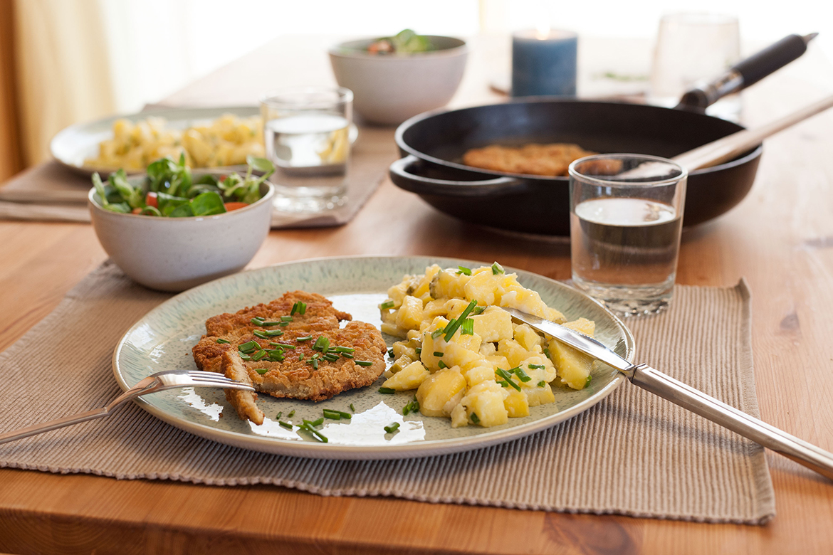 De veganistische schnitzel van seitan ligt op een bord met een portie aardappelsalade.
