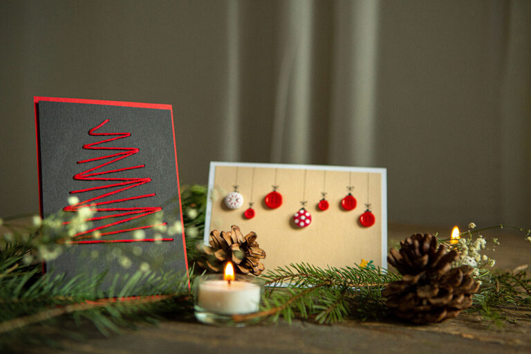 Twee zelfgemaakte kerstkaarten staan op een kerstversierde tafel.