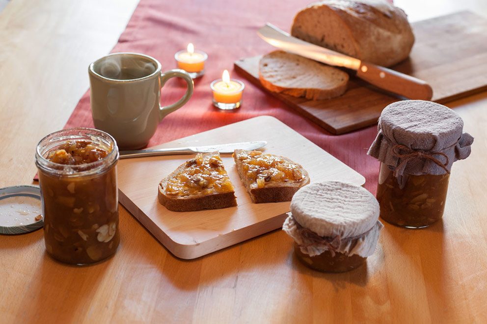 Drie potten gepofte appeljam staan op de ontbijttafel, een snee brood is besmeerd met de jam.