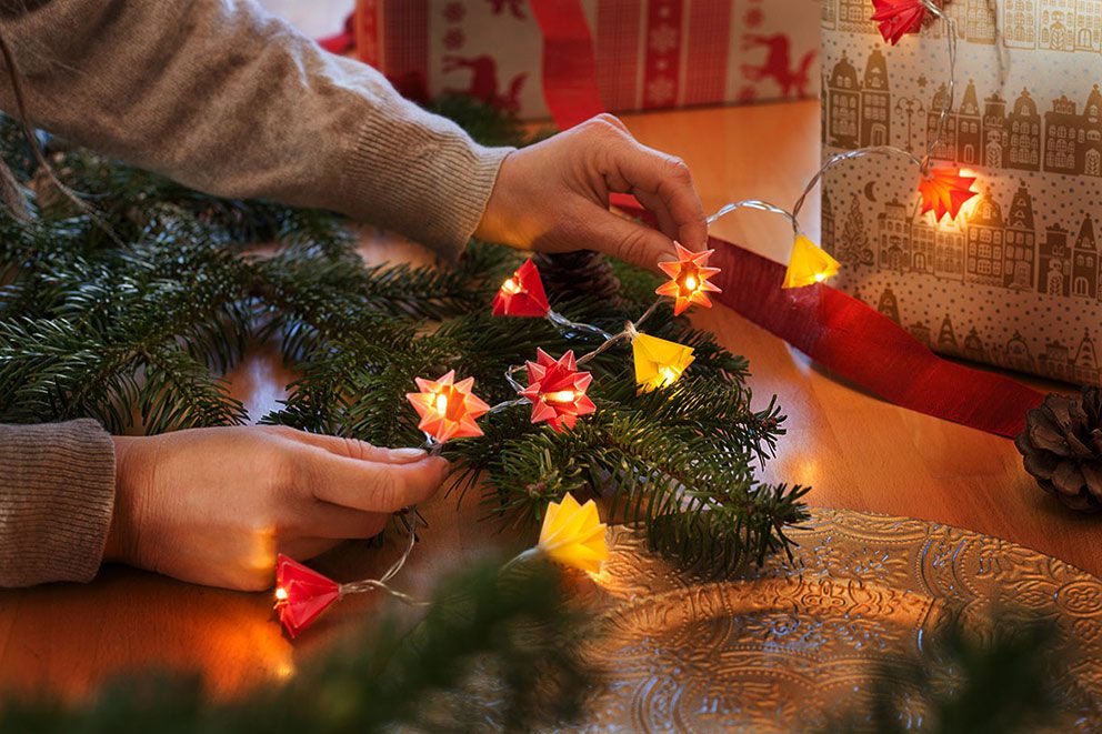 De voltooide lichtketting wordt door een vrouw op groene dennentakken gedrapeerd.