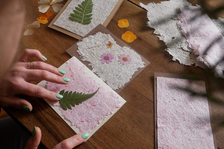 Een vrouw maakt kaarten van het handgeschepte papier, dat ze versiert met gedroogde planten.