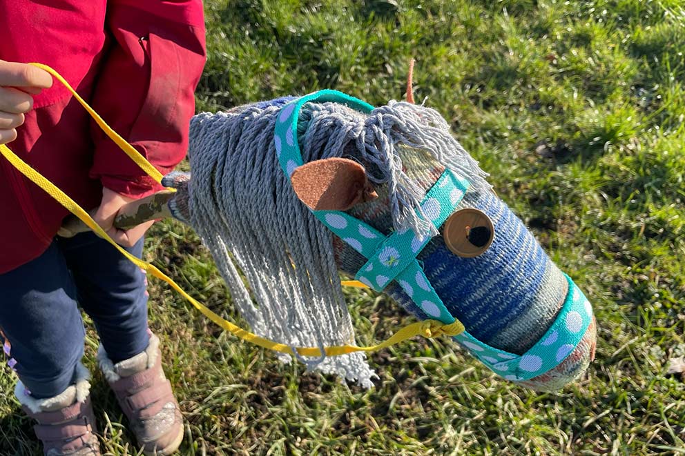 Een klein meisje speelt met een stokpaardje in een groene weide.