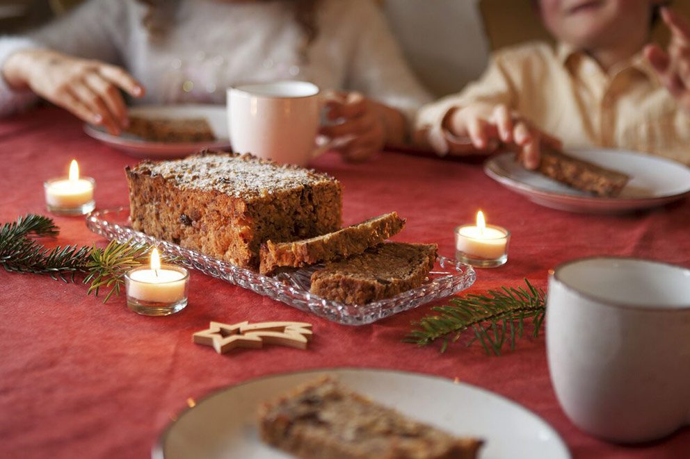 Het vers gebakken vruchtenbrood staat op een gedekte tafel met een rood tafelkleed en brandende kaarsen.