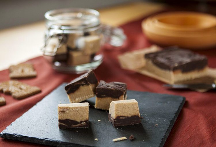 De speculaasfudge ligt op een leistenen plank met een glas zelfgemaakte fudge op de achtergrond.