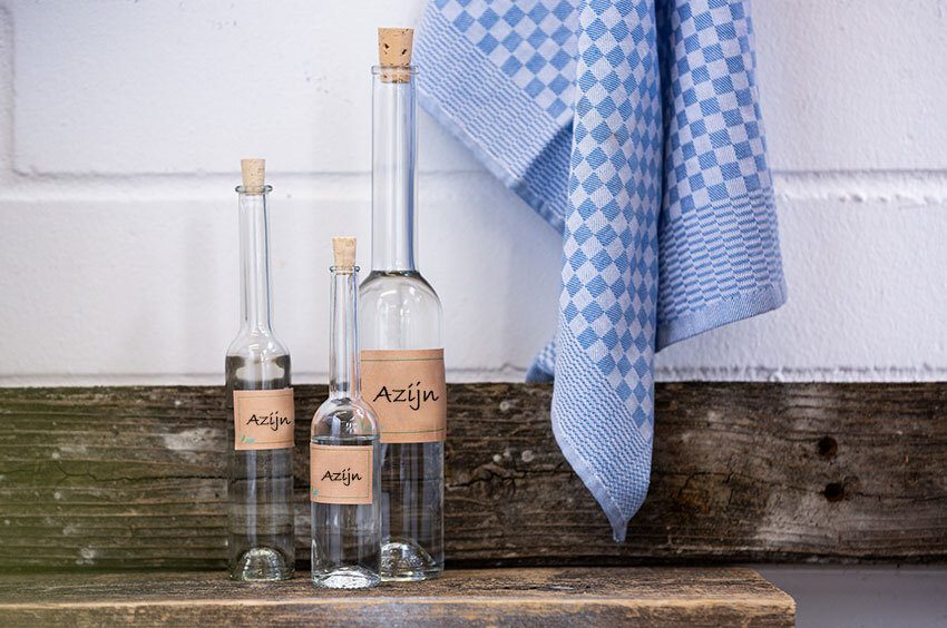 Drie azijnflessen van verschillende groottes staan op een houten plank.