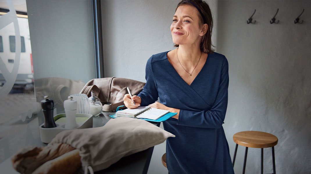Vrouw in biologische wollen jurk zit in een café en schrijft in een notitieboekje