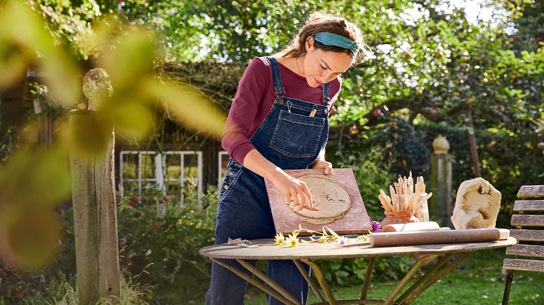 Vrouw in kleding van bio-katoen is aan het pottenbakken in de tuin