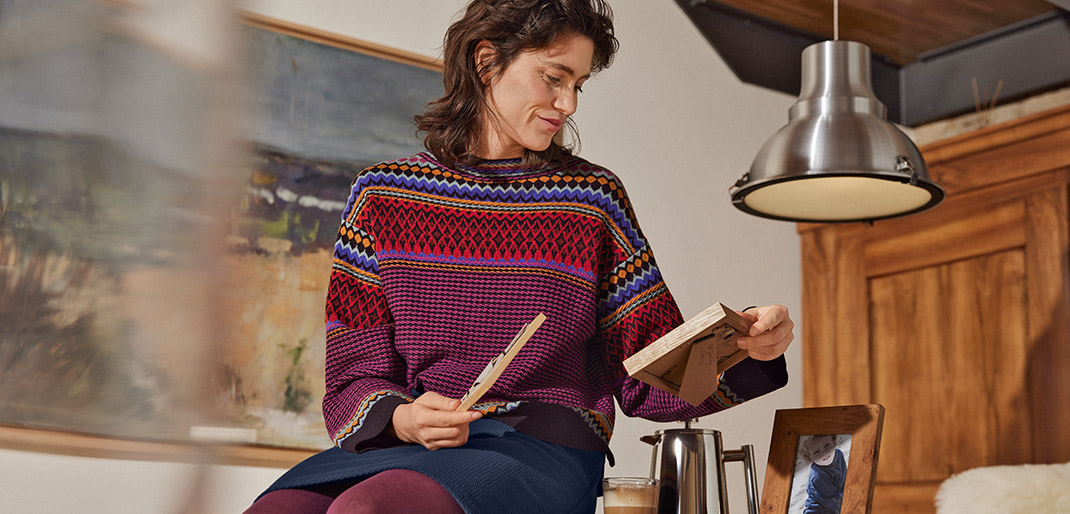 Vrouw draagt een gebreide jacquard trui, zit op een tafel en kijkt naar een foto.