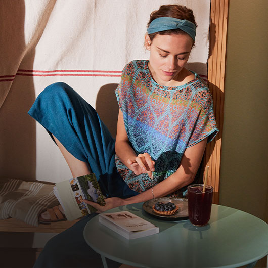 Vrouw in jacquard-mode zit in een café.