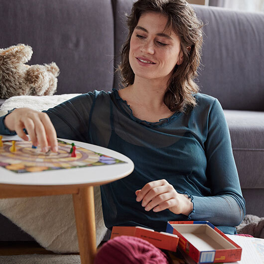 Vrouw in een biologisch zijden shirt zit in de woonkamer en speelt een bordspel