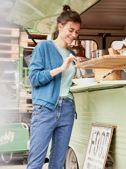 Vrouw in een overgangsjas van bio-wol staat bij een foodtruck