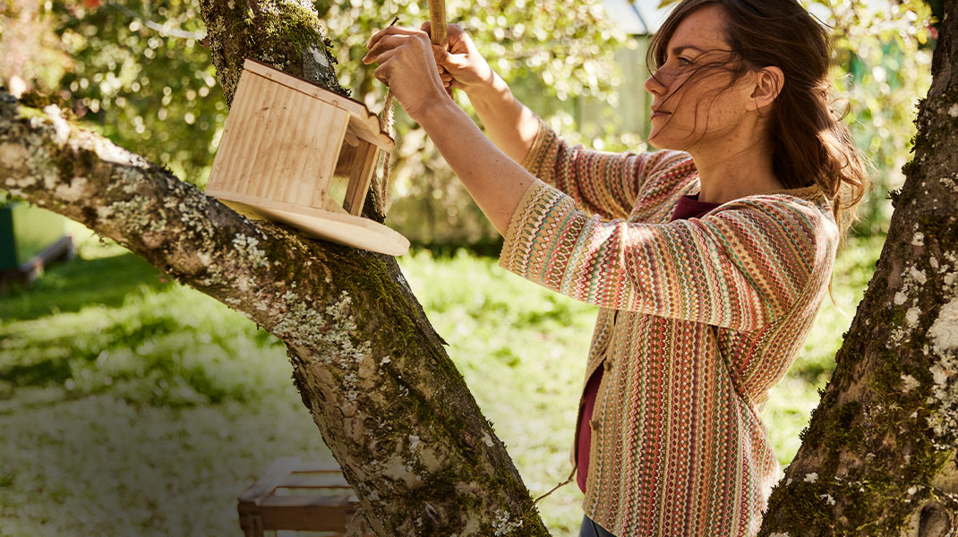 Vrouw hangt een voederstation op in een boom in haar bio-tuin