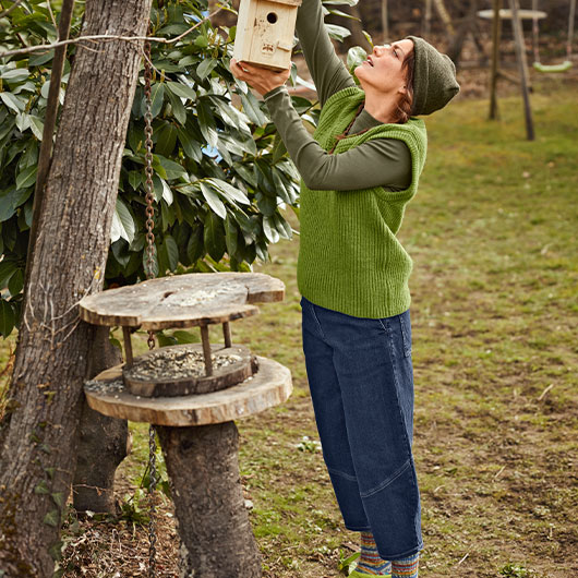 Vrouw hangt een vogelhuisje op voor de winter.