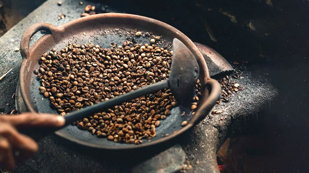 Gebrande koffiebonen in kleikom met vuurvaste pollepel
