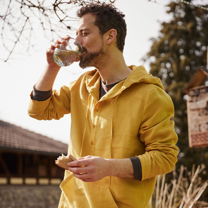 Man in linnen shirt drinkt in de tuin.