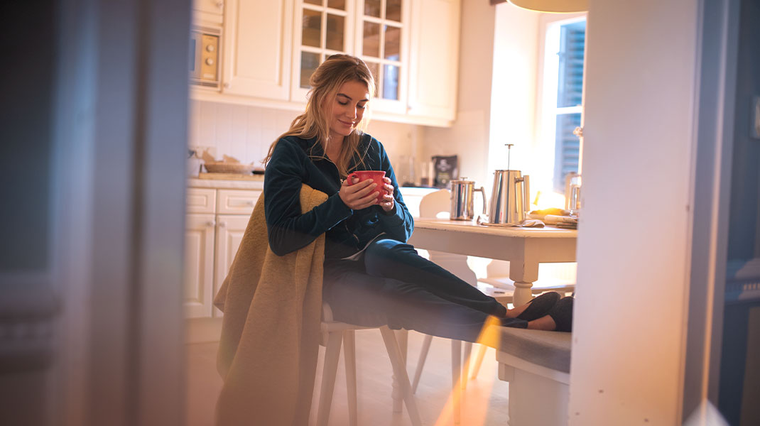 Vrouw zit 's morgens in de keuken in comfortabele kleding en drinkt een koffie.