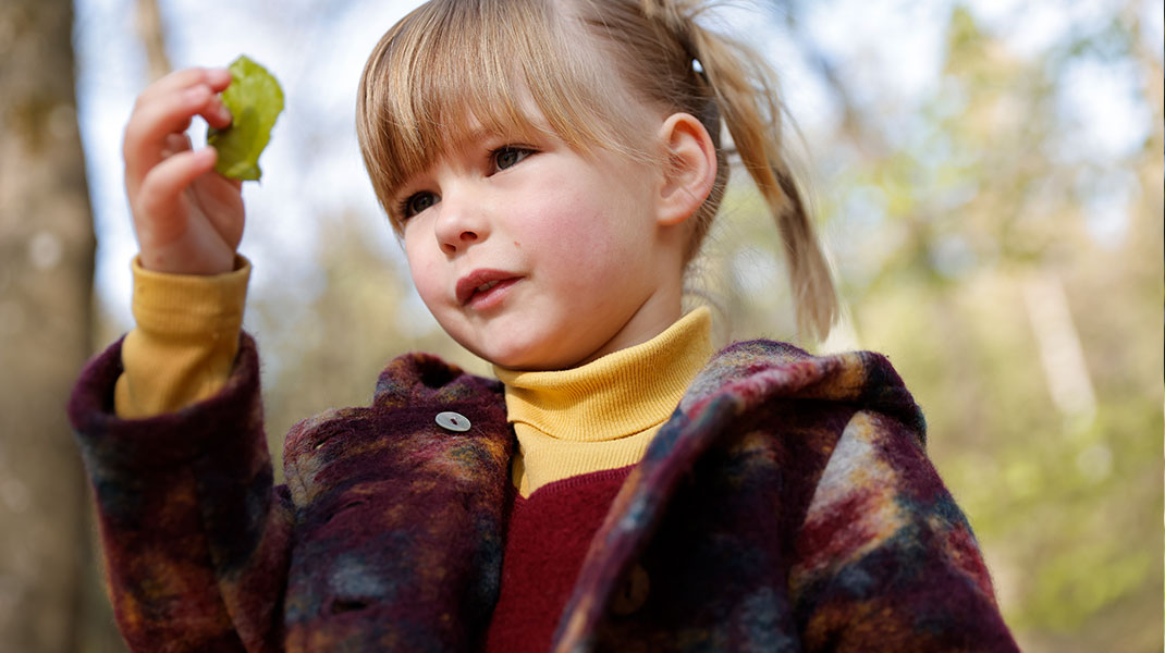 Meisje in kleurrijke mantel van bio-walkstof kijkt naar een blaadje