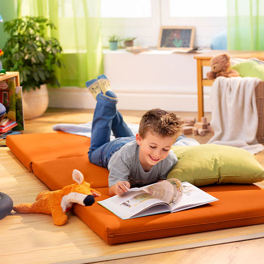 Jongen leest liggen op een oranje matras in een duurzaam ingerichte kamer