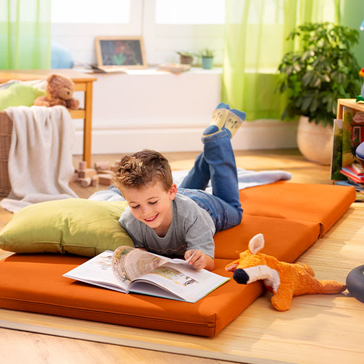 Jongen leest liggen op een oranje matras in een duurzaam ingerichte kamer