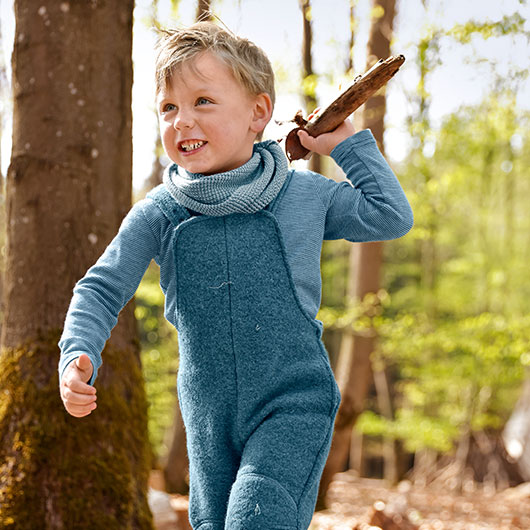 Jongen in het bos draagt een blauwe tuinbroek van bio-walkstof