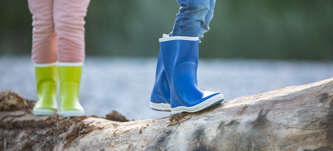 Kinderen balanceren op een boomtam in regenlaarzen