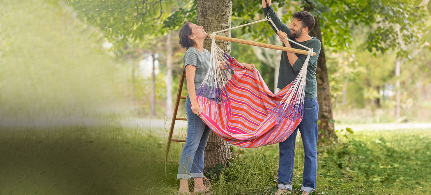Man en vrouw bevestigen een hangstoel aan een boom in de natuurlijke tuin
