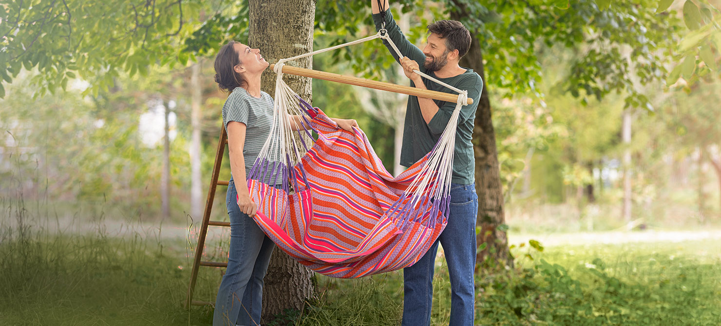 Man en vrouw bevestigen een hangstoel aan een boom in de natuurlijke tuin