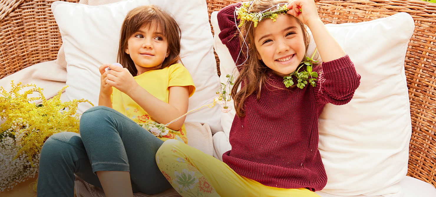 Kinderen dragen bio-mode van Waschbär en spelen met bloemen op een rieten bank