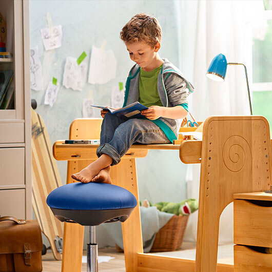 Jongen zit op een verstelbaar bureau in een duurzaam ingerichte kinderkamer.